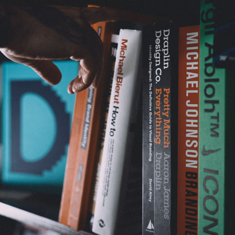 A hand pulling a book from a shelf of branding and design titles.