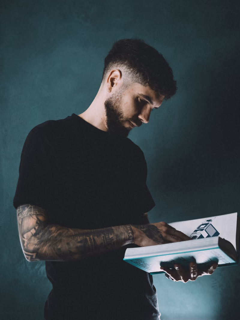 Ethan Suero standing against a dark green wall, reading a design book.
