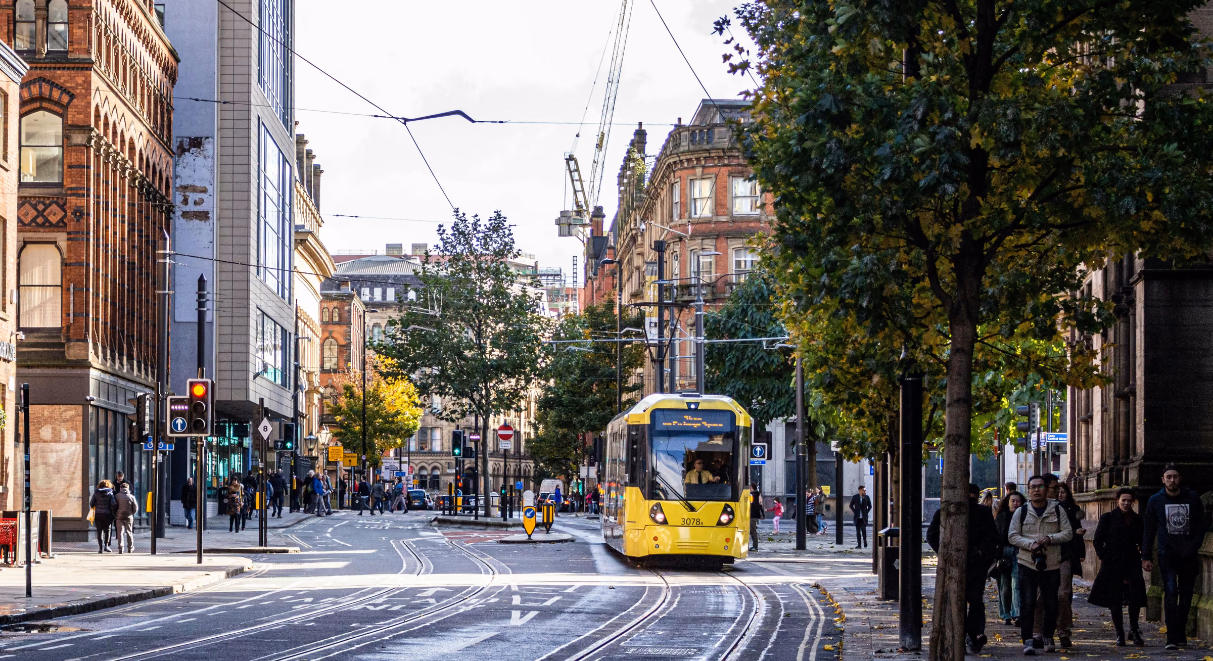 A yellow Metrolink tram running through Manchester city centre.